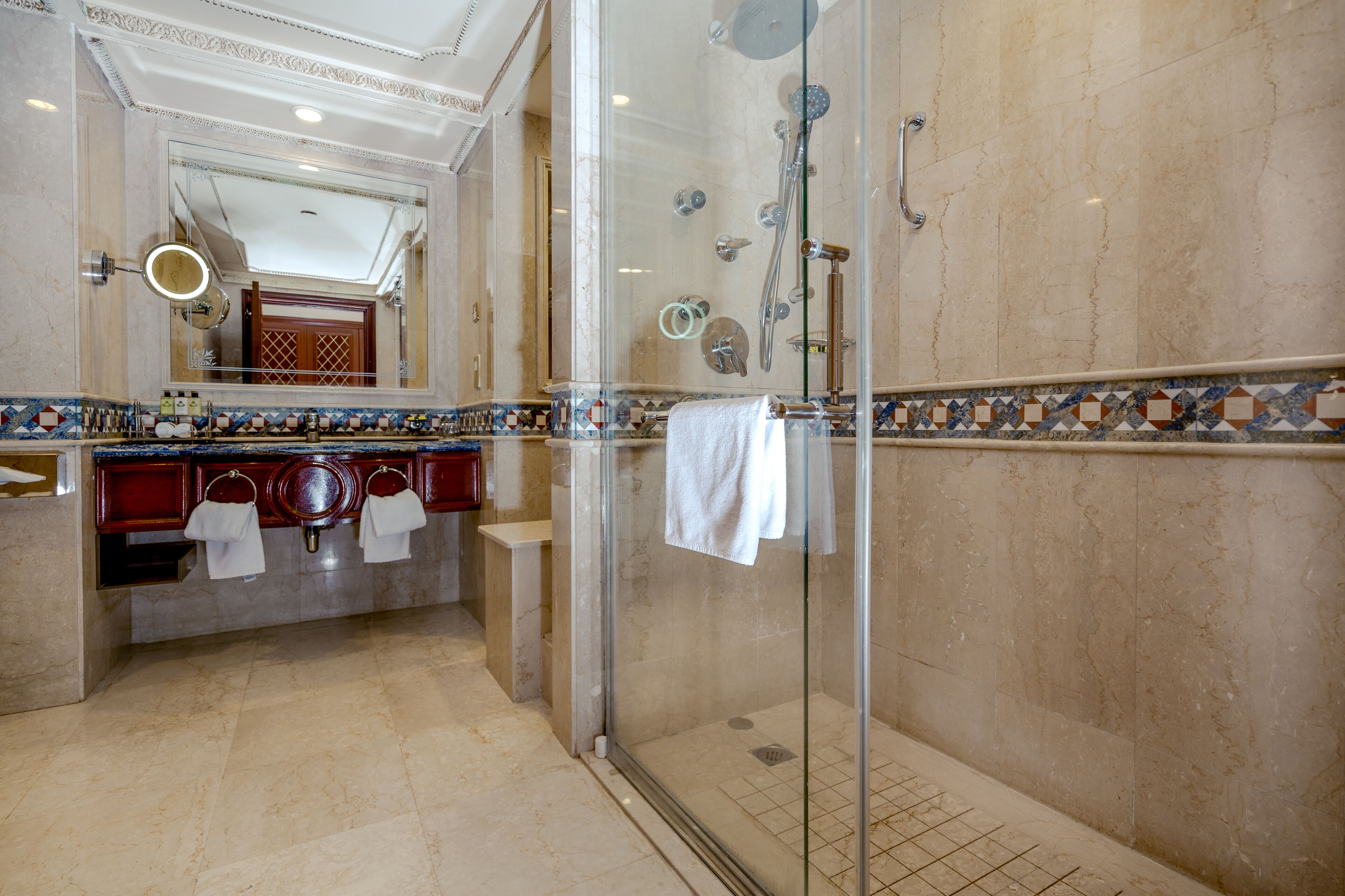 Une salle de bain luxueuse dotée d’une douche à parois de verre, d’un sol carrelé en marbre et d’un meuble-lavabo avec un miroir et un porte-serviettes.