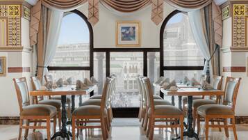 A dining area with tables set for six, large arched windows, and traditional decor.