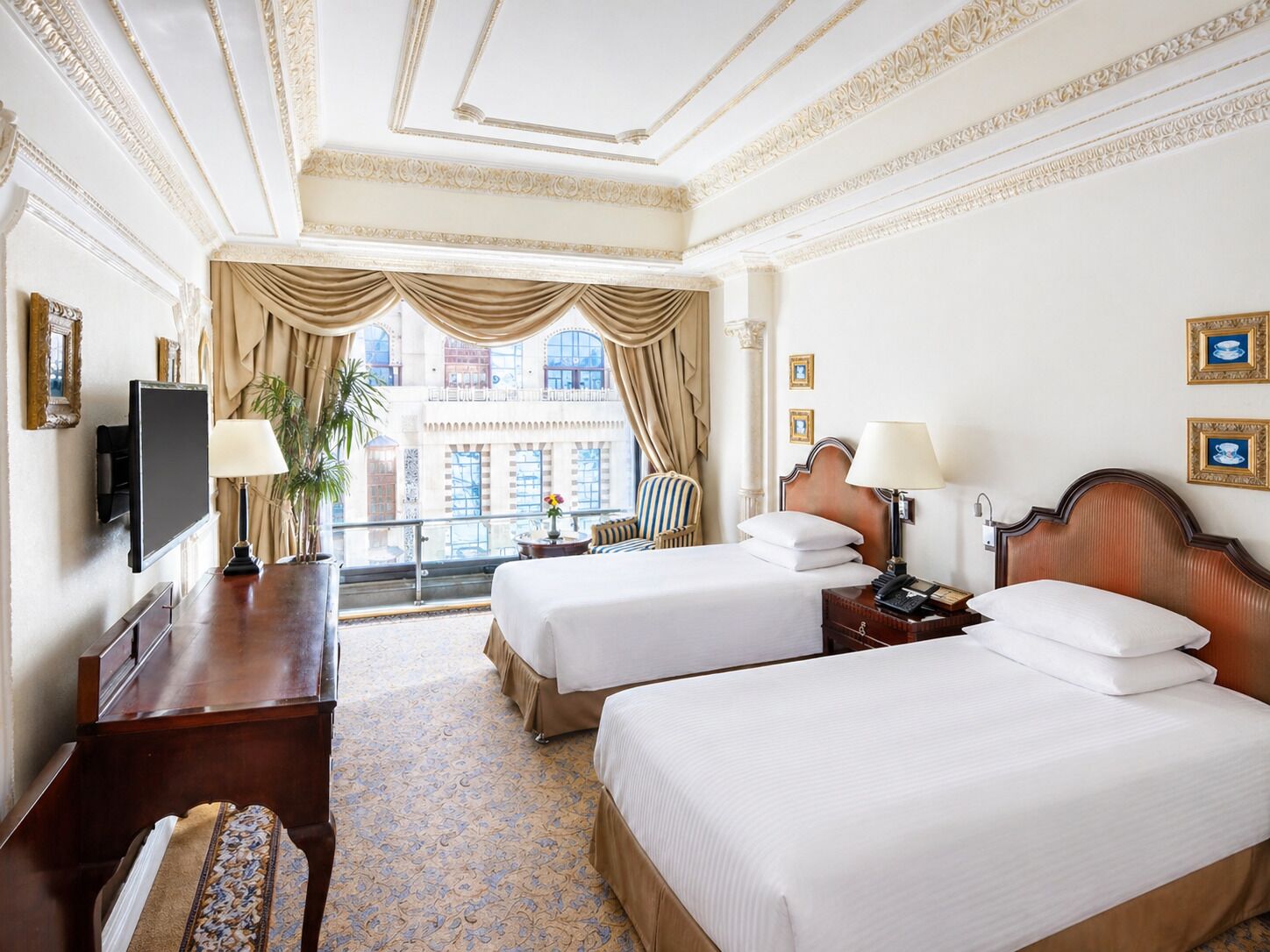 A hotel room with two beds, a TV, a desk, a chair, and a balcony with curtains.