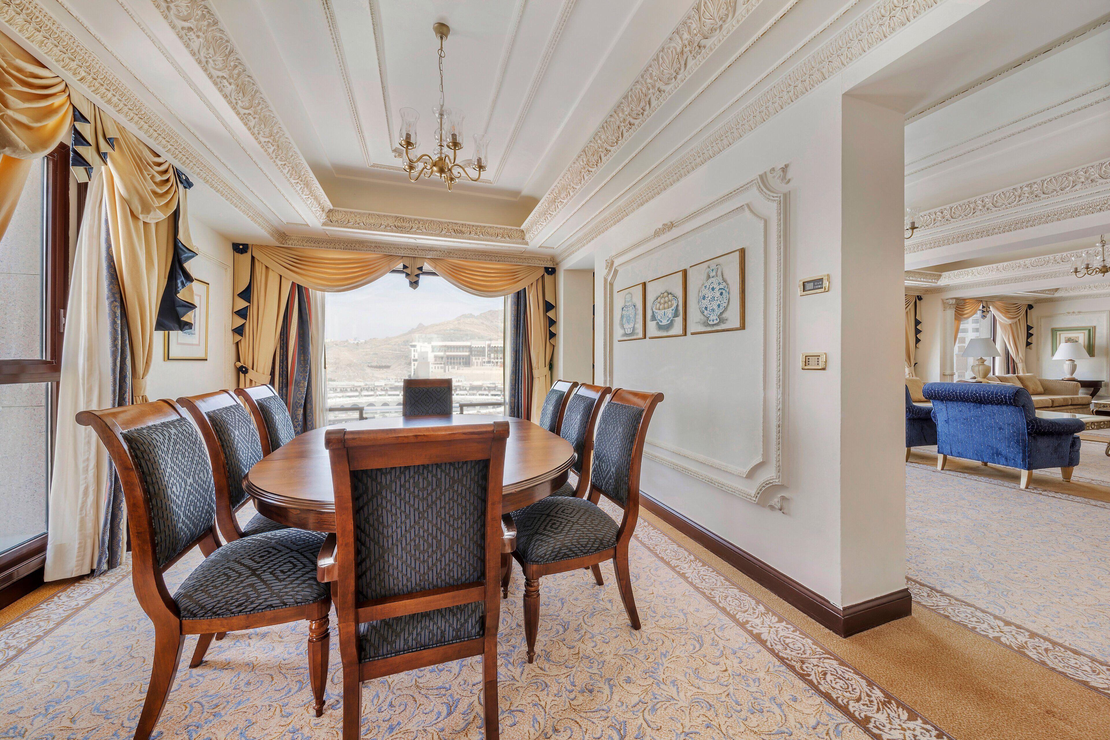 A formal dining room with a round table, six upholstered chairs, and a patterned carpet.