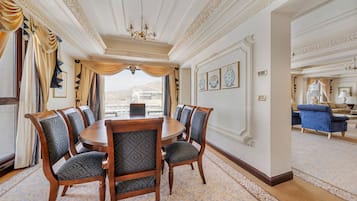 A formal dining room with a round table, six upholstered chairs, and a patterned carpet.