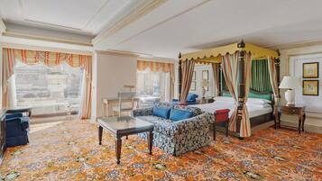 A hotel room with a large window, a four-poster bed, a sofa, a coffee table, and a patterned carpet.