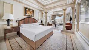 Une chambre spacieuse avec un grand lit, un plafond décoré et une vue sur l’extérieur, visible à travers une porte en arc de cercle.