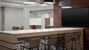 A modern kitchen with a large island, bar stools, pendant lighting, and a flat-screen TV mounted on the wall.