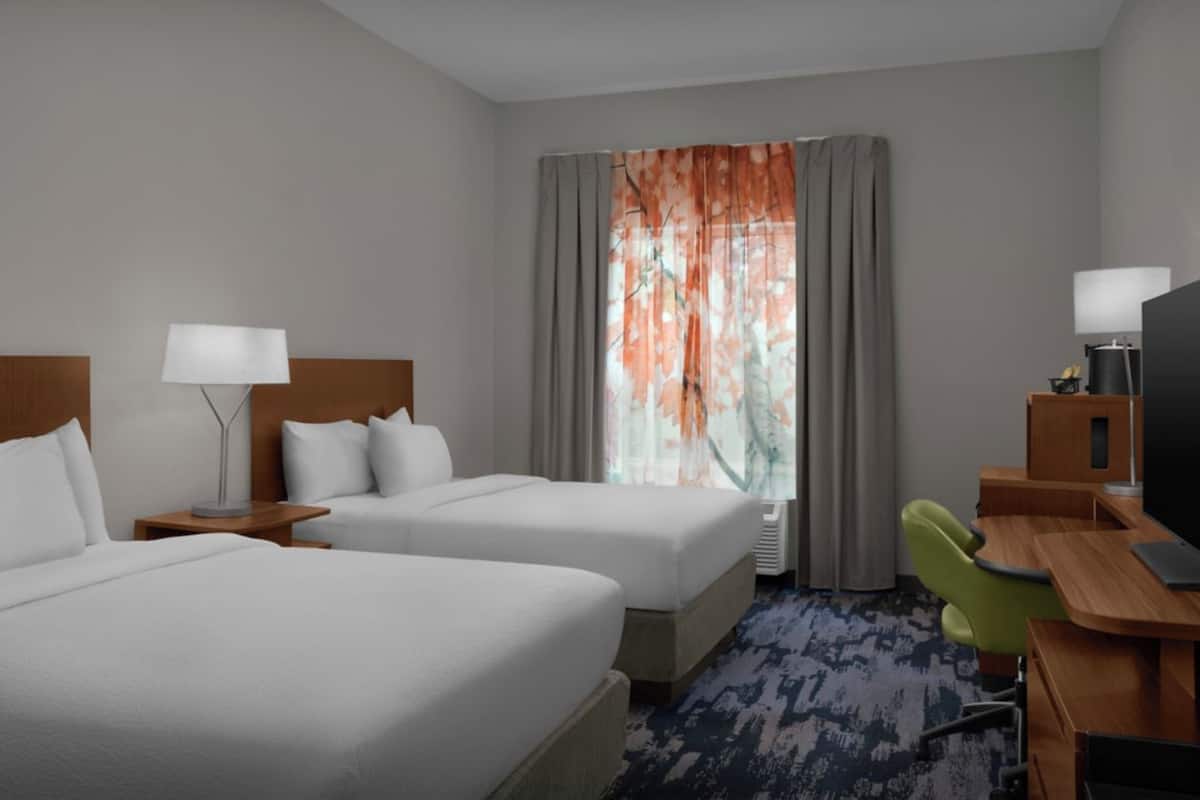 A hotel room with two beds, a desk with a chair, a television, and a window with curtains.