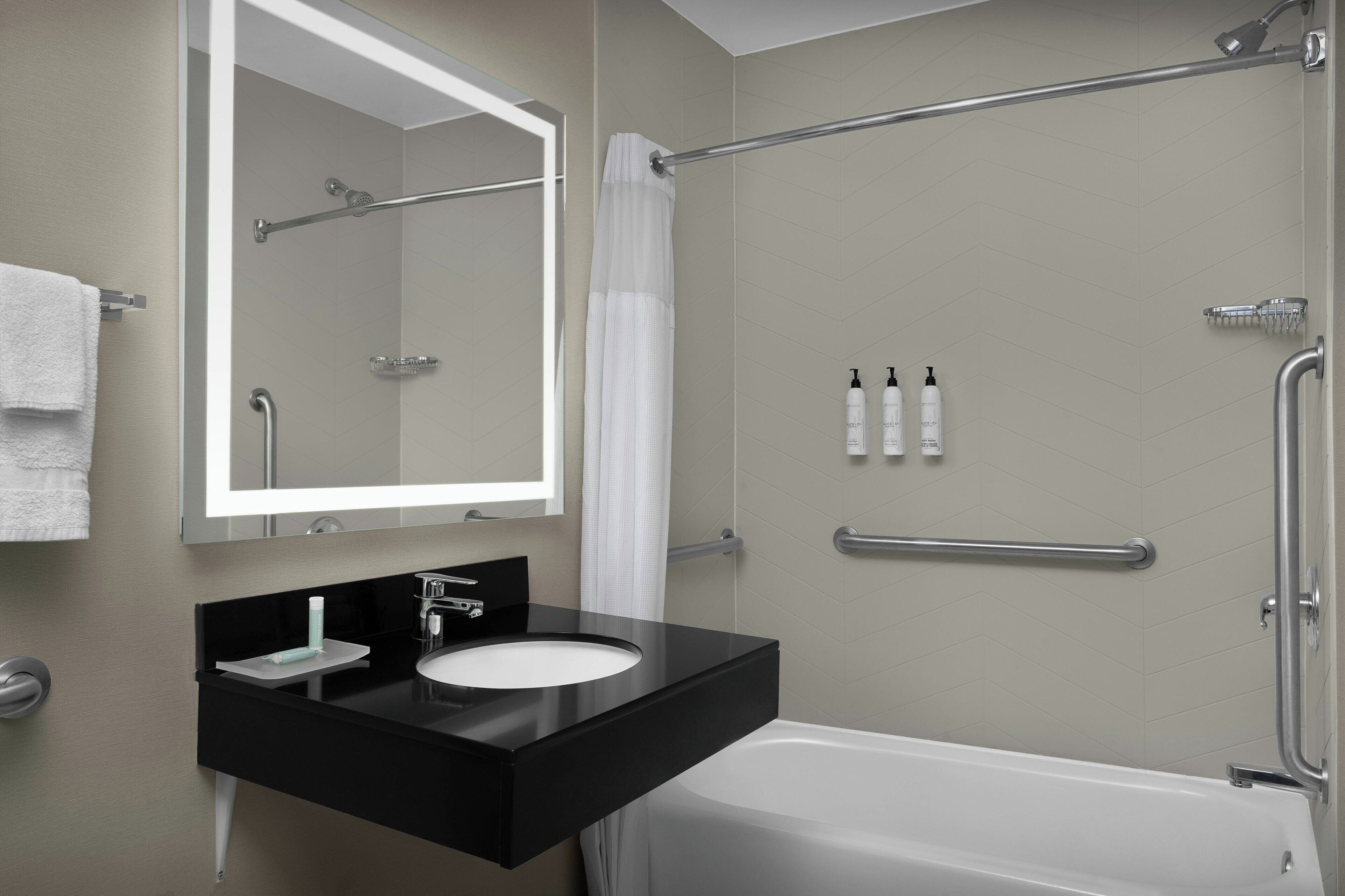 Un baño moderno con un tocador negro, lavamanos blanco y un espejo grande.