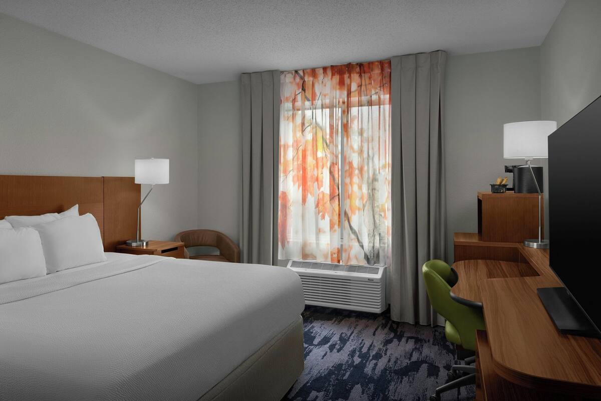 A hotel room with a bed, a desk, a chair, a television, and a window with curtains.