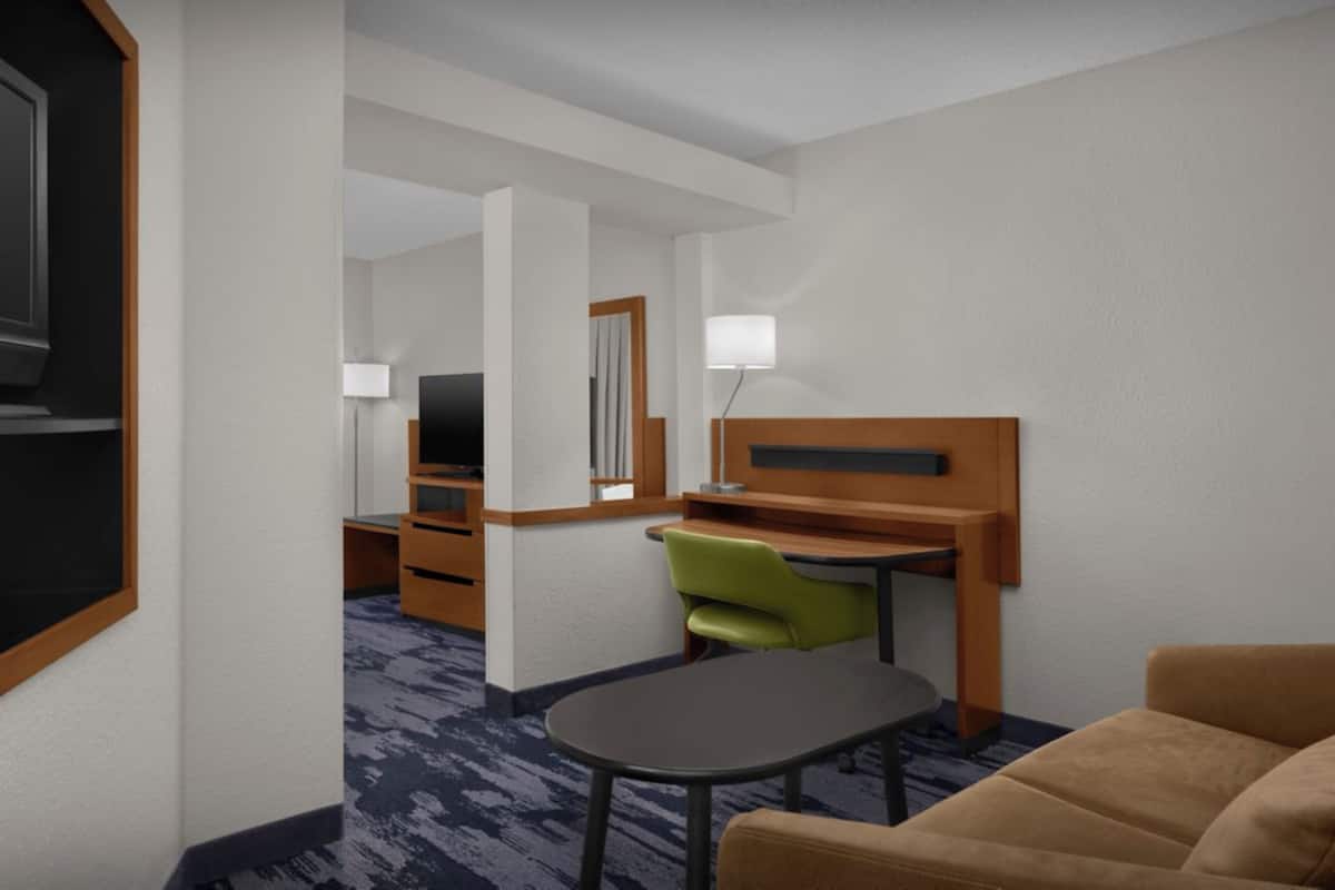 A hotel room with a bed, a desk, a chair, a lamp, and a television.