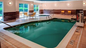 An indoor swimming pool with a tiled floor, a wooden bench area, and a seating arrangement with chairs.
