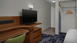 A hotel room with a wooden desk, a television, a green chair, a wardrobe, a coat rack with hangers, and a door leading to another room.