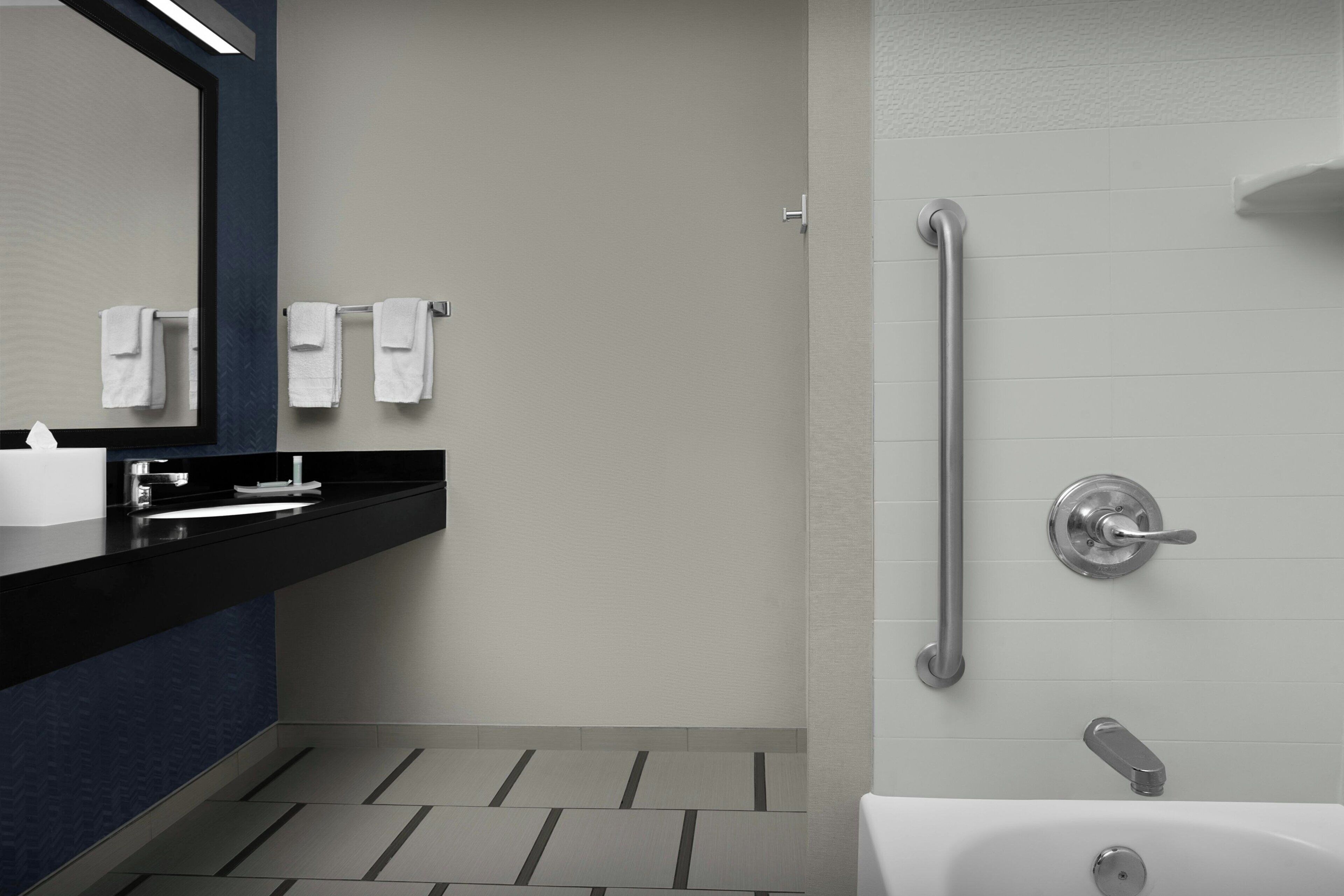A modern bathroom with a black countertop, a large mirror, and a walk-in shower with a grab bar.