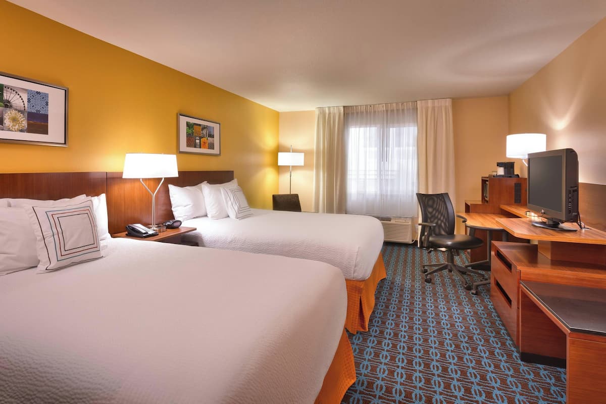 Een hotelkamer met twee bedden, een bureau, een stoel, een televisie en een lamp.