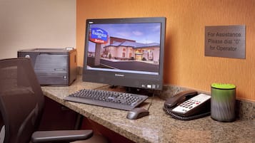 A hotel reception desk with a computer monitor displaying the Fairfield Inn & Suites sign, a desk phone, a keyboard, a mouse, and a trash can.