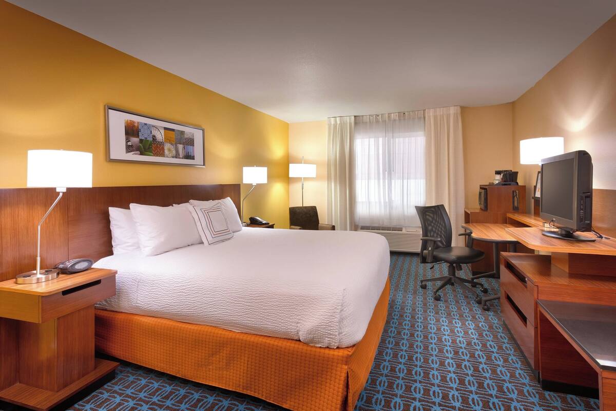 Een hotelkamer met een groot bed, een bureau met een computer, een televisie en een stoel.