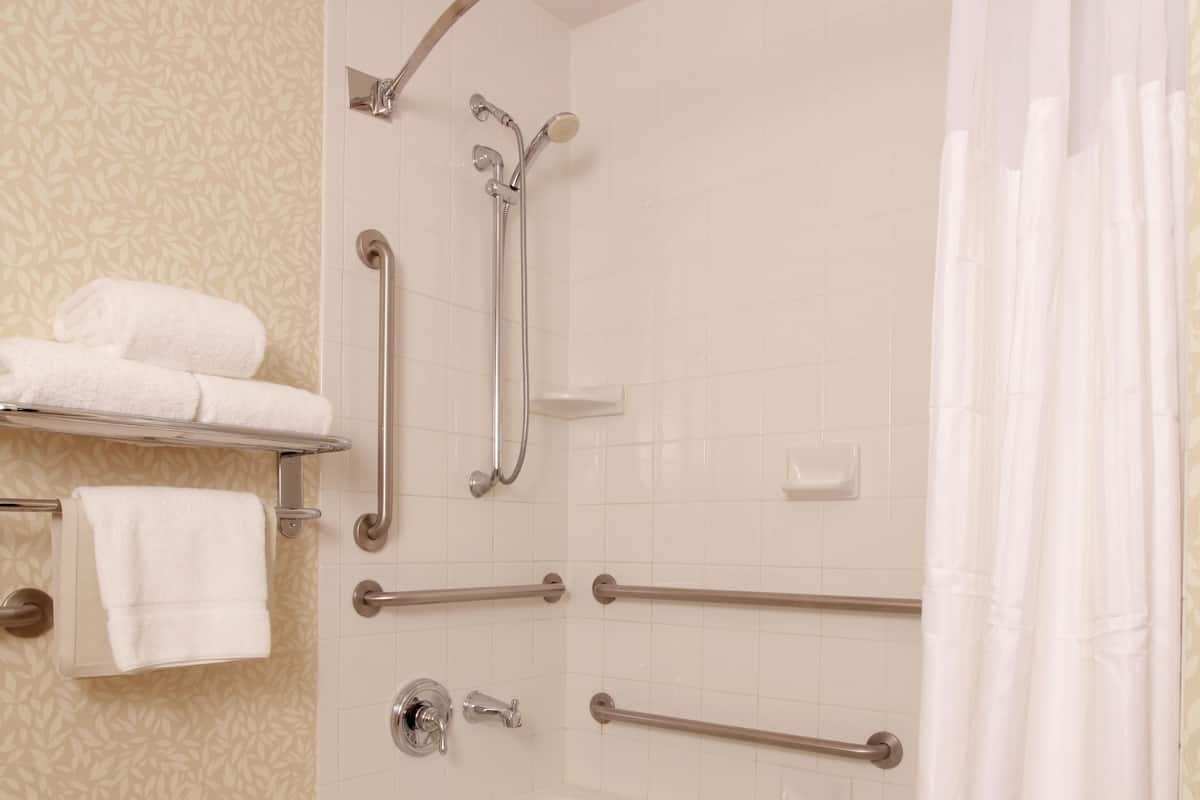 A bathroom with a bathtub, grab bars, a towel rack, and a shower curtain.