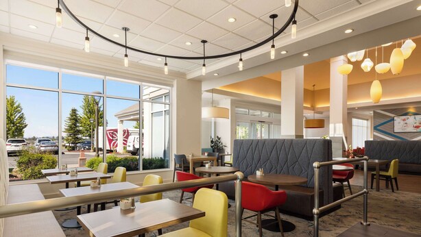 A modern indoor space with tables and chairs, large windows, and a seating area with a cushioned bench. - Hilton Garden Inn Spokane Airport (Spokane)