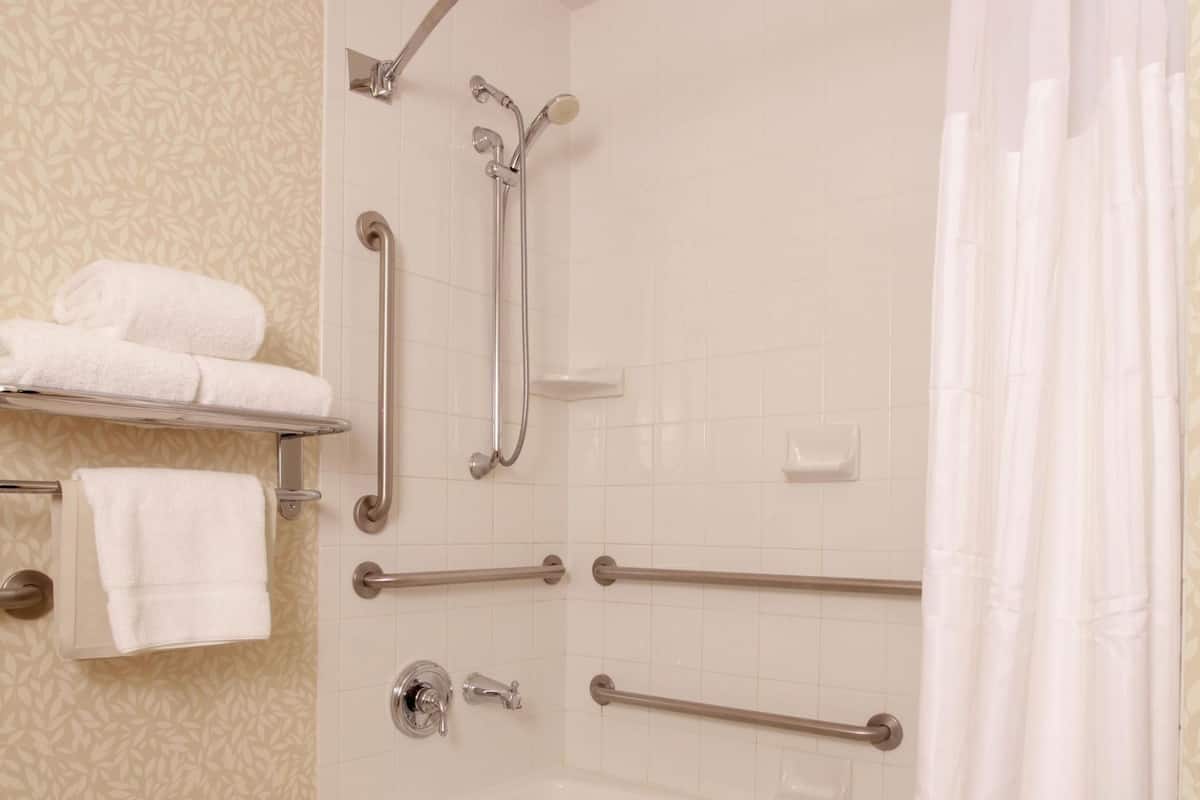 A bathroom with a bathtub, grab bars, a towel rack, and a shower curtain.