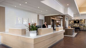 A hotel reception area with a modern design, including a reception desk, a seating area, and a bar/lounge with a television. - Hilton Garden Inn Spokane Airport (Spokane)