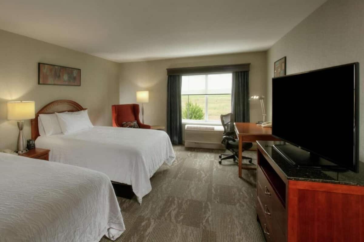 A hotel room with two beds, a desk with a television, a chair, and a window with a view.