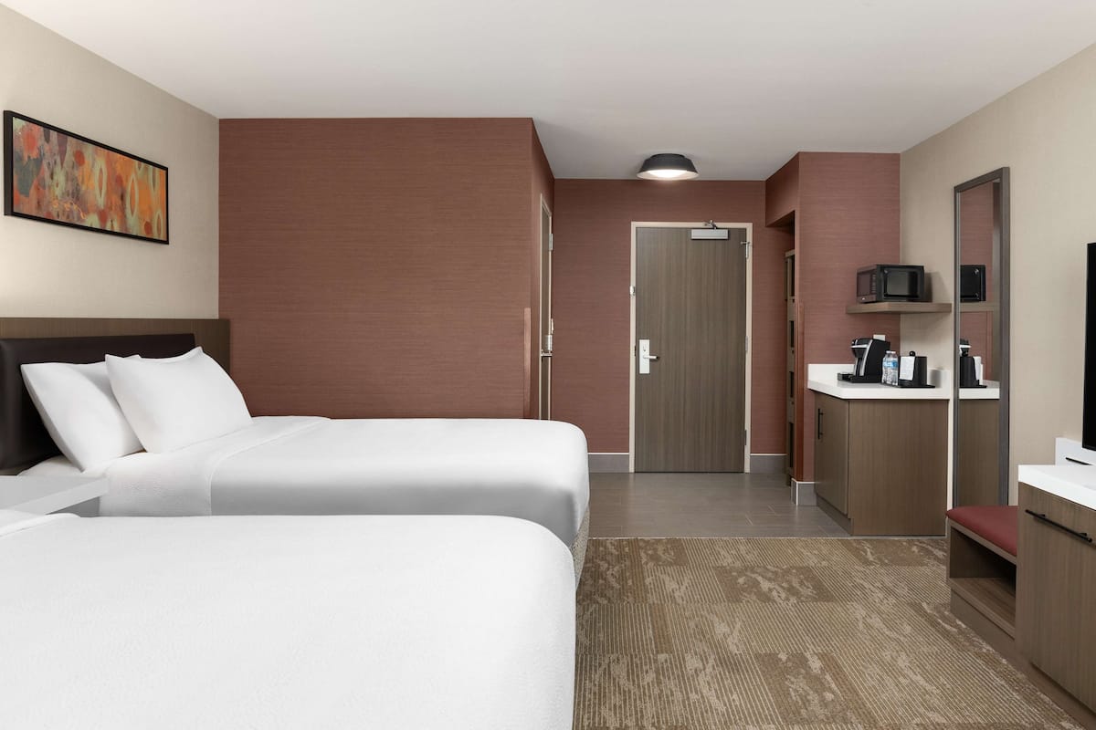 A hotel room with two beds, a bathroom, a microwave, a coffee maker, and a TV.