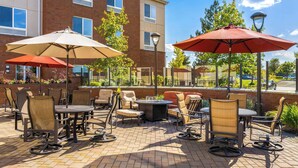 An outdoor patio with brick flooring, multiple tables and chairs, and two large umbrellas providing shade. - Hilton Garden Inn Spokane Airport (Spokane)