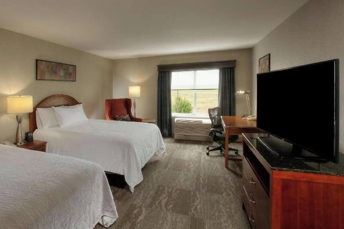 A hotel room with two beds, a desk, a television, and a window with curtains.