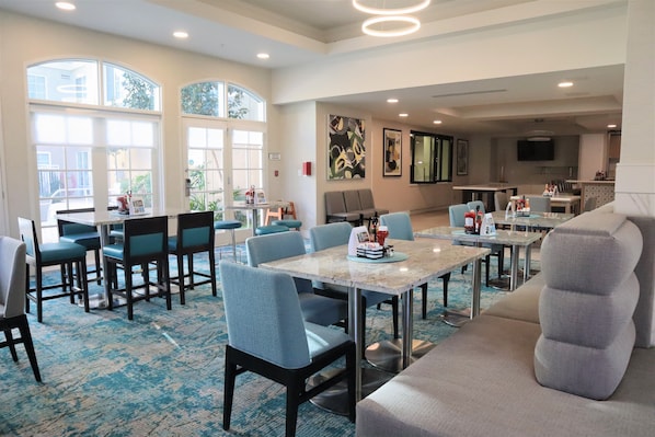 A hotel dining area with tables and chairs, a large window, and artwork on the walls.