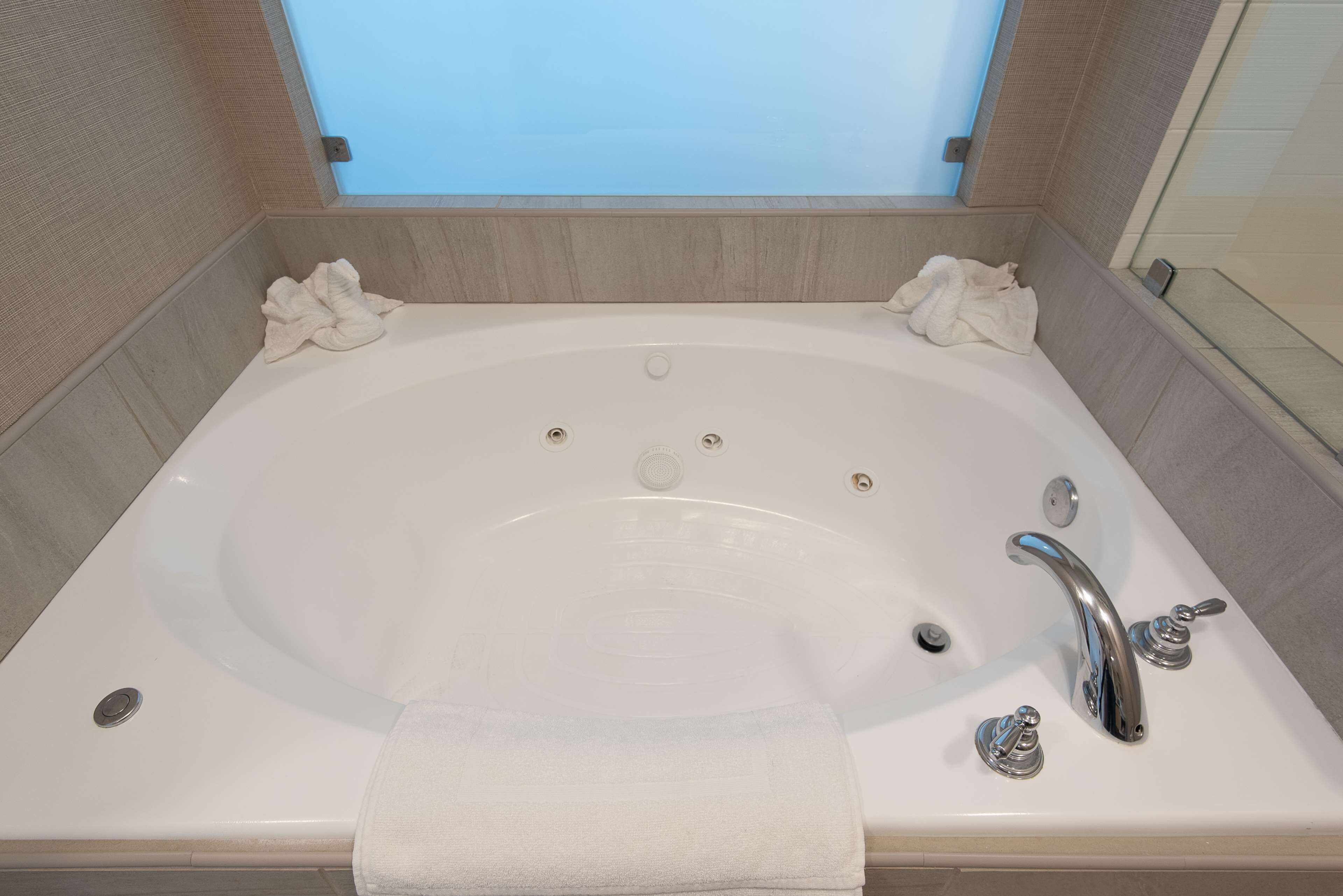 A large, rectangular bathtub with two faucets and a drain, surrounded by beige tiles.