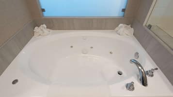 A large, rectangular bathtub with two faucets and a drain, surrounded by beige tiles.