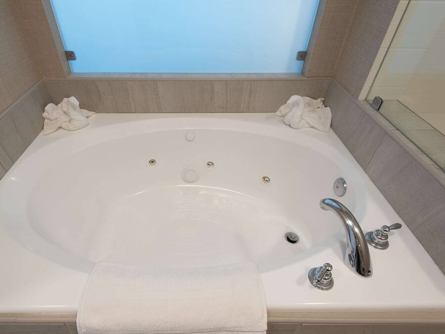 Une grande baignoire rectangulaire, dotée de deux robinets et d’un drain, et entourée de carreaux de couleur beige.