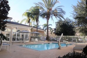 A pool area with lounge chairs, a palm tree, and a building with large windows.