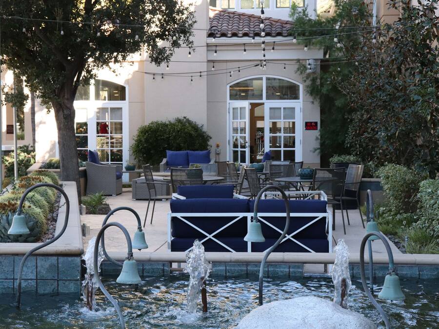 An outdoor pool area with a fountain, seating, and a building with a tiled roof in the background.