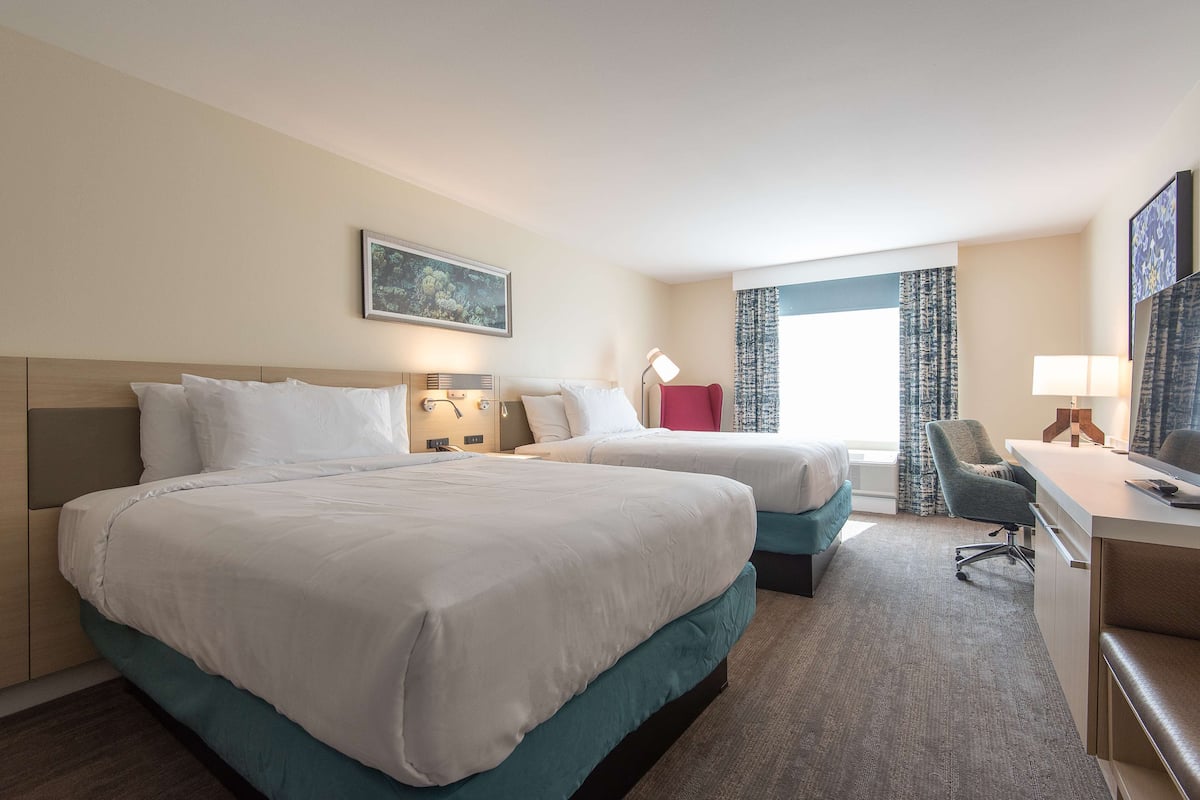 A hotel room with two beds, a desk, a chair, and a window with curtains.