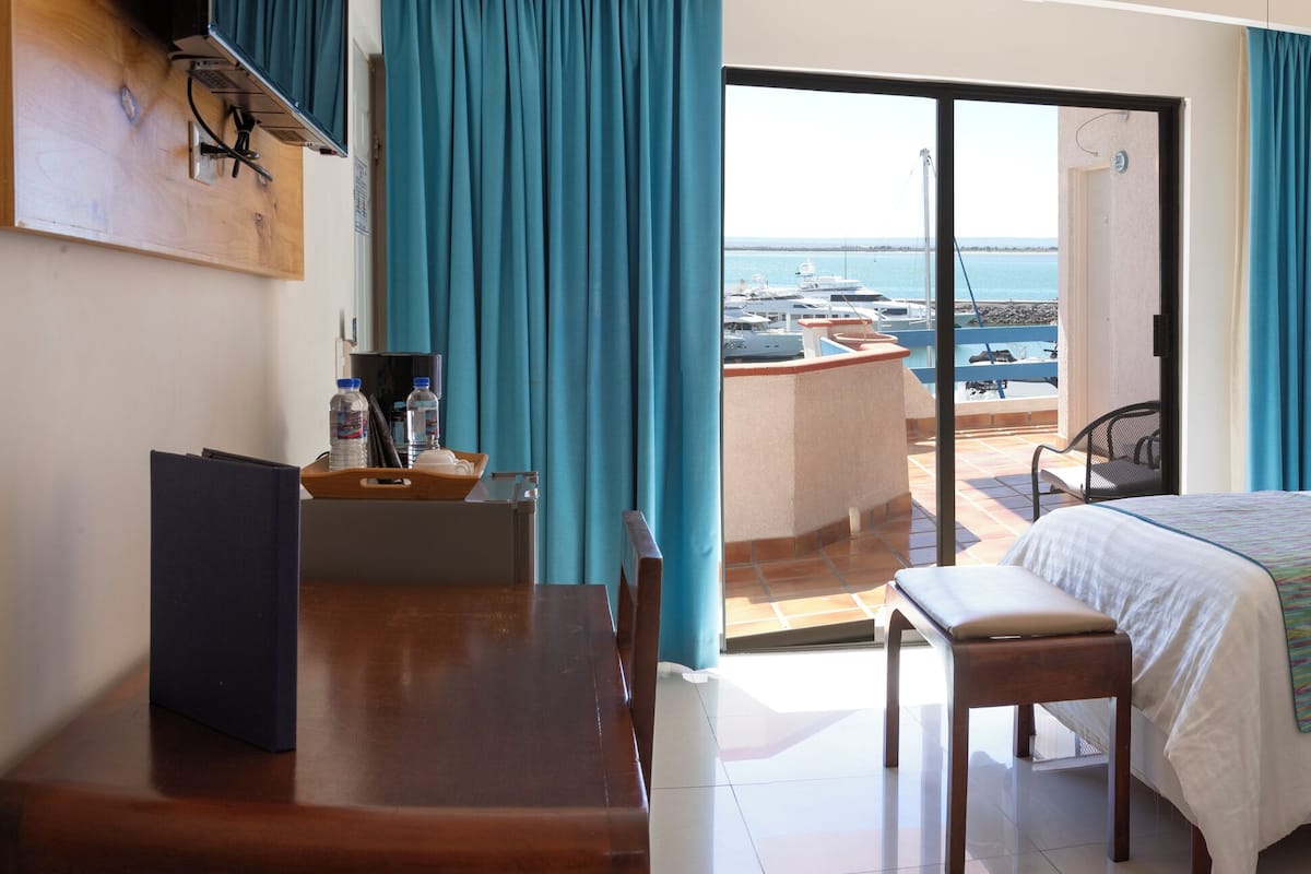 Ett hotellrum med två sängar, ett skrivbord, en stol och utsikt över havet.