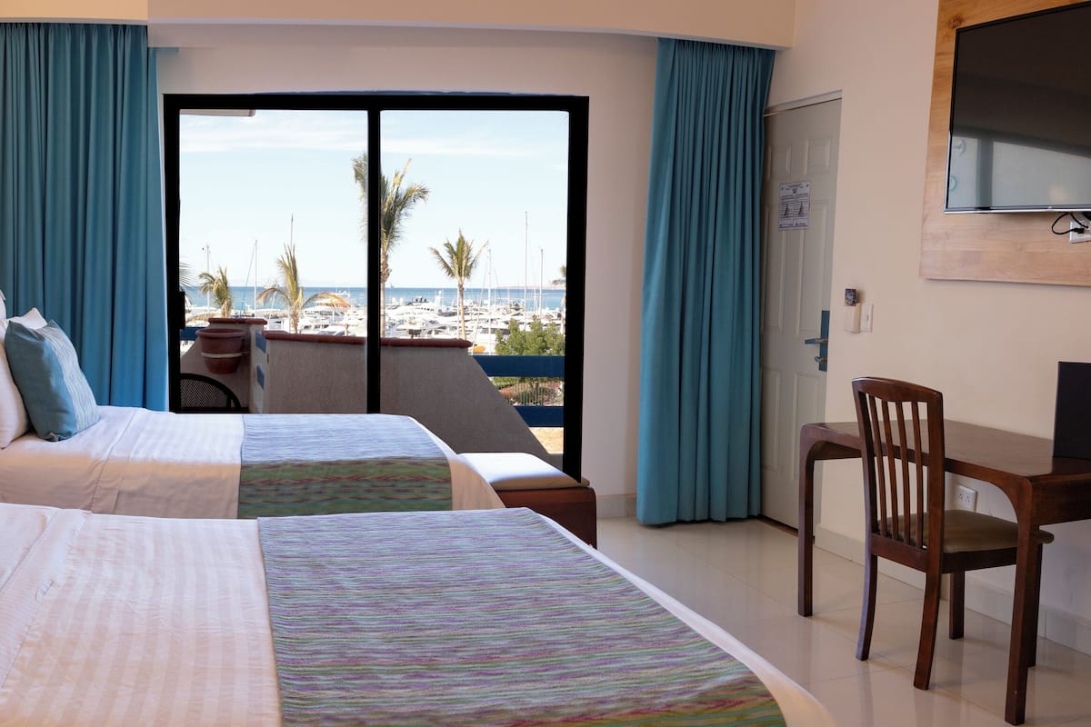 Ett hotellrum med två sängar, en TV, ett skrivbord och utsikt över stranden.
