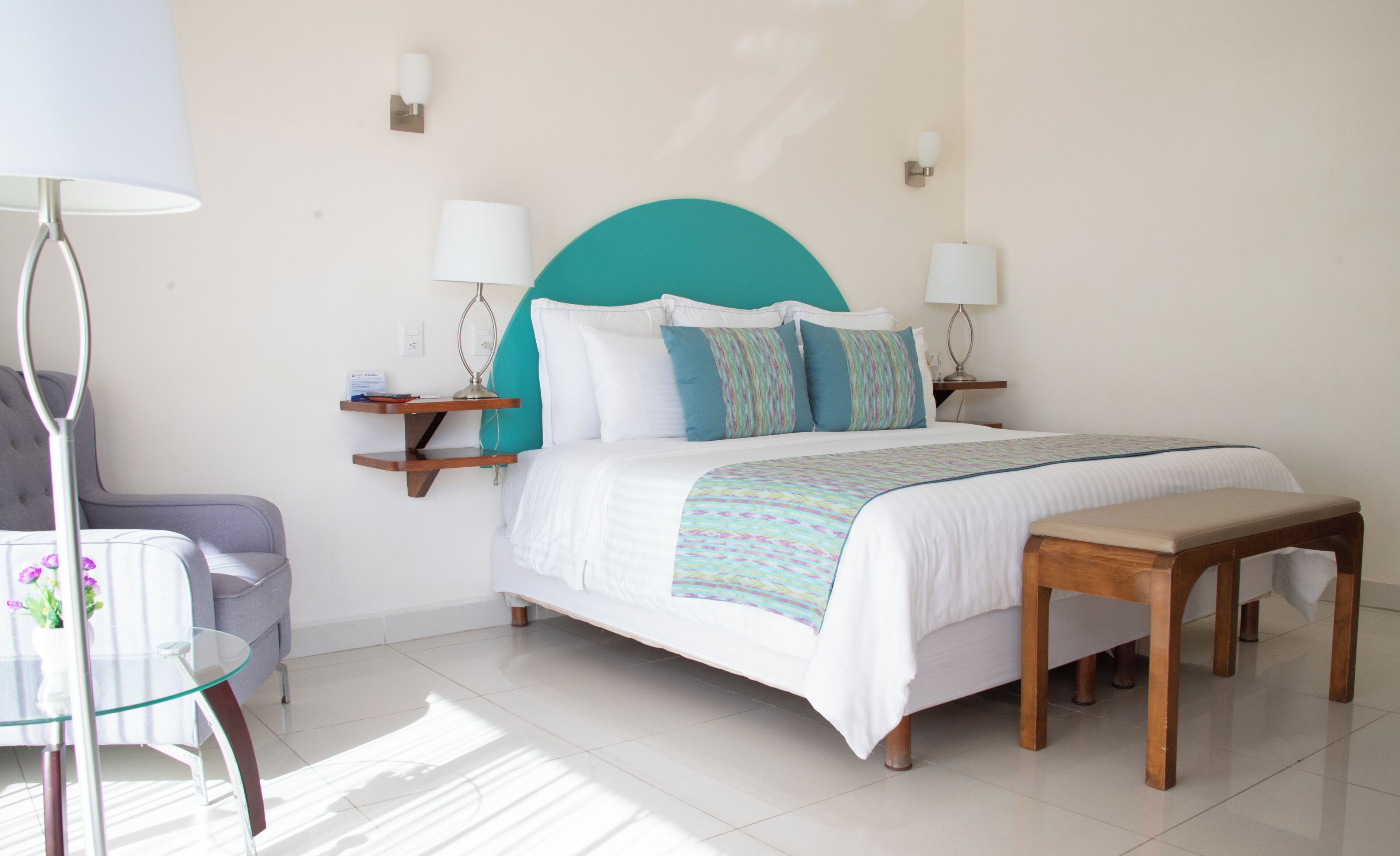 Una habitación de hotel ordenada con una cama, mesitas de noche, una silla y una lámpara.