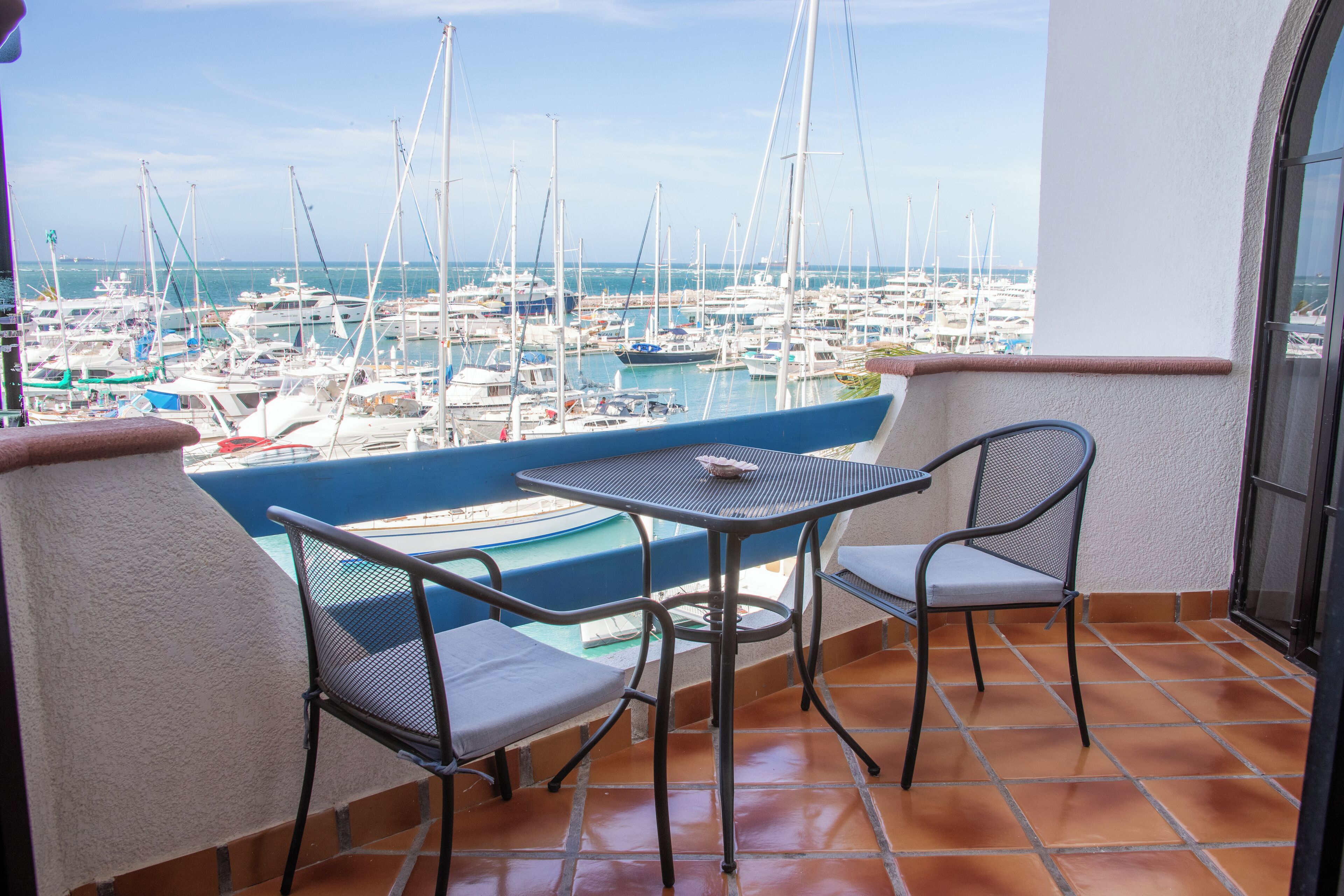 Un balcón con vista a un puerto deportivo, con una mesa y dos sillas.