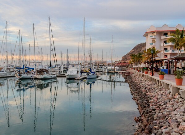 Un port de plaisance où sont amarrés de nombreux bateaux, une côte rocheuse et un bâtiment doté de balcons et d’une terrasse.