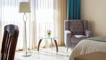 A hotel room with a bed, a grey armchair, a glass table with a vase of flowers, and a floor lamp.