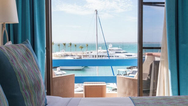 A hotel room with a large window offering a view of a marina and the sea. - The Westmarine Waterfront Hotel (La Paz)