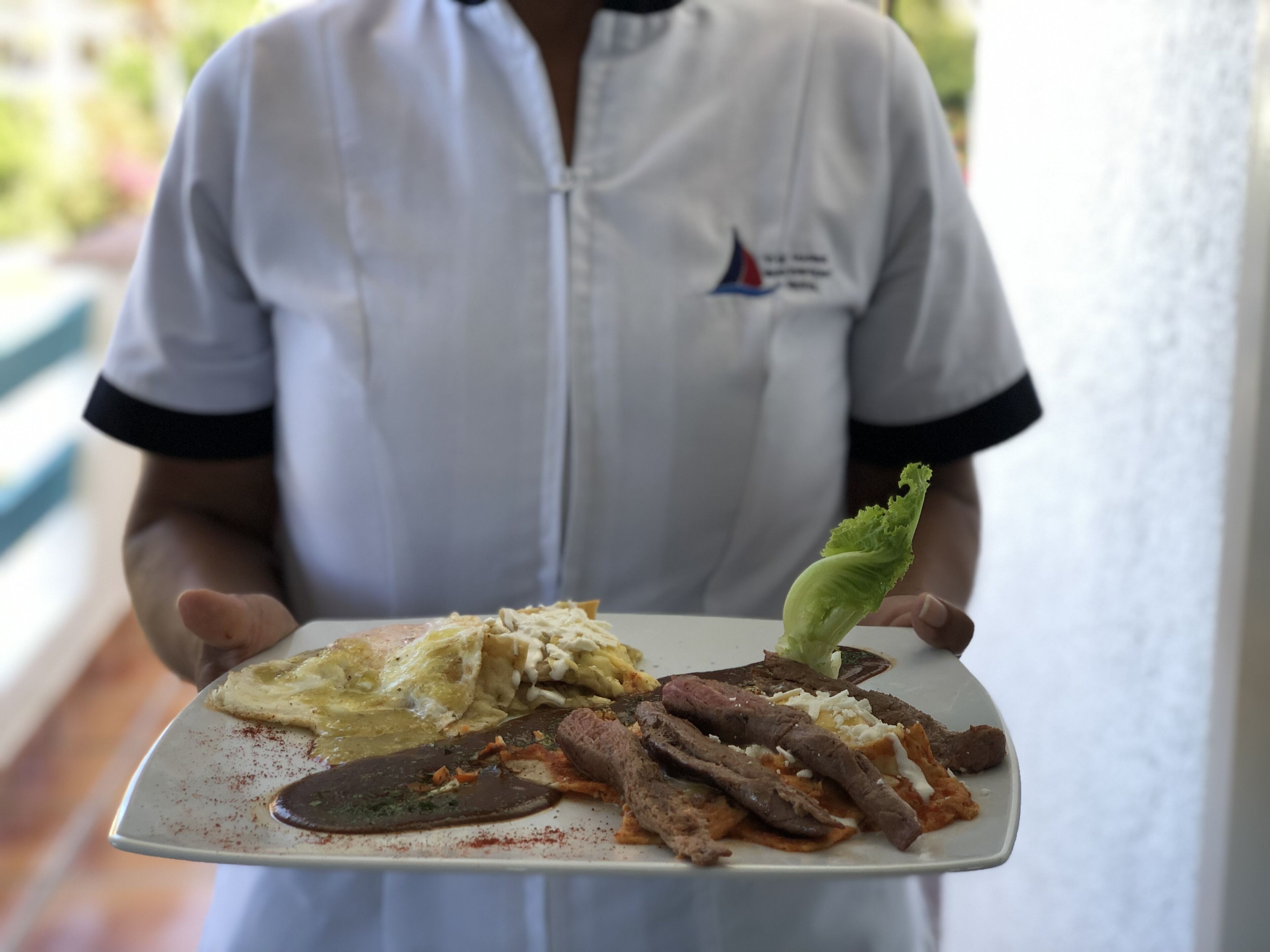 A person holding a plate with various food items, including a salad, eggs, and meat.