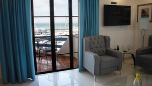 A living room with a large window, a grey armchair, a glass coffee table, and a flat-screen TV on the wall. - The Westmarine Waterfront Hotel (La Paz)