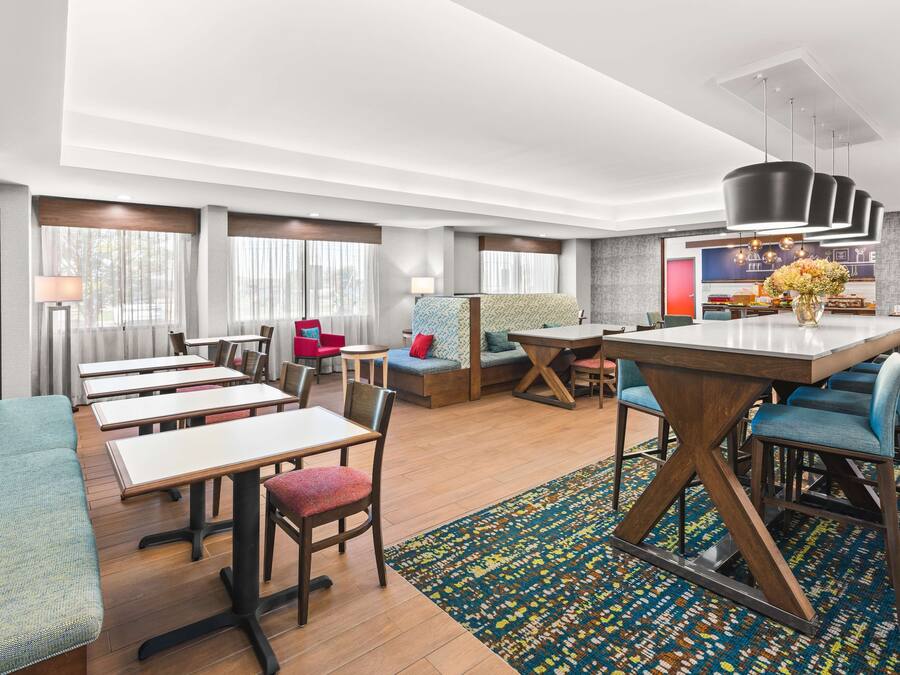 A modern hotel lobby with a central dining area, multiple seating options including sofas and chairs, and a reception desk.