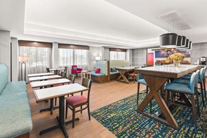 Un moderno vestíbulo de hotel con un área de comedor central, múltiples opciones de asientos, incluyendo sofás y sillones, y una recepción.