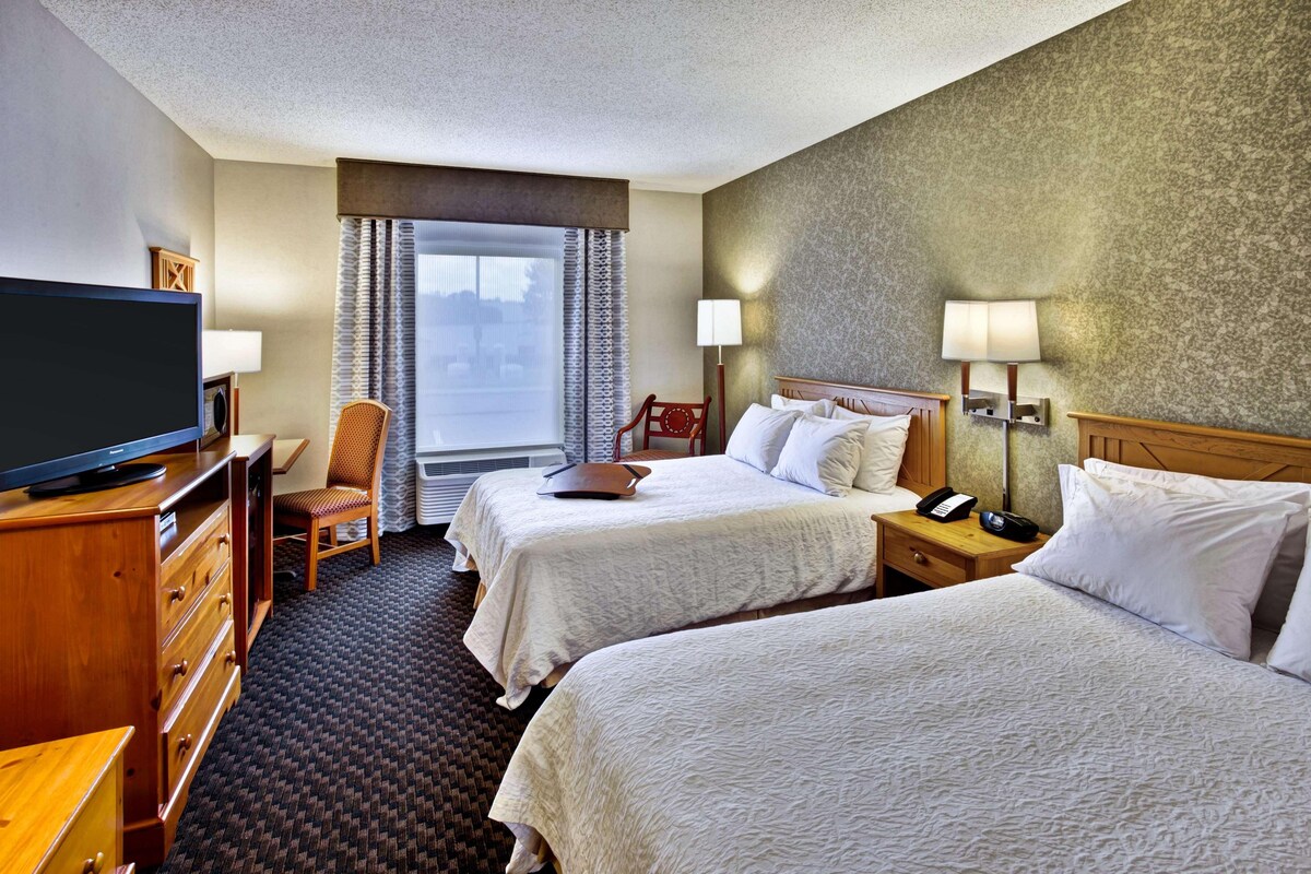 A hotel room with two beds, a TV, a desk, and a chair.