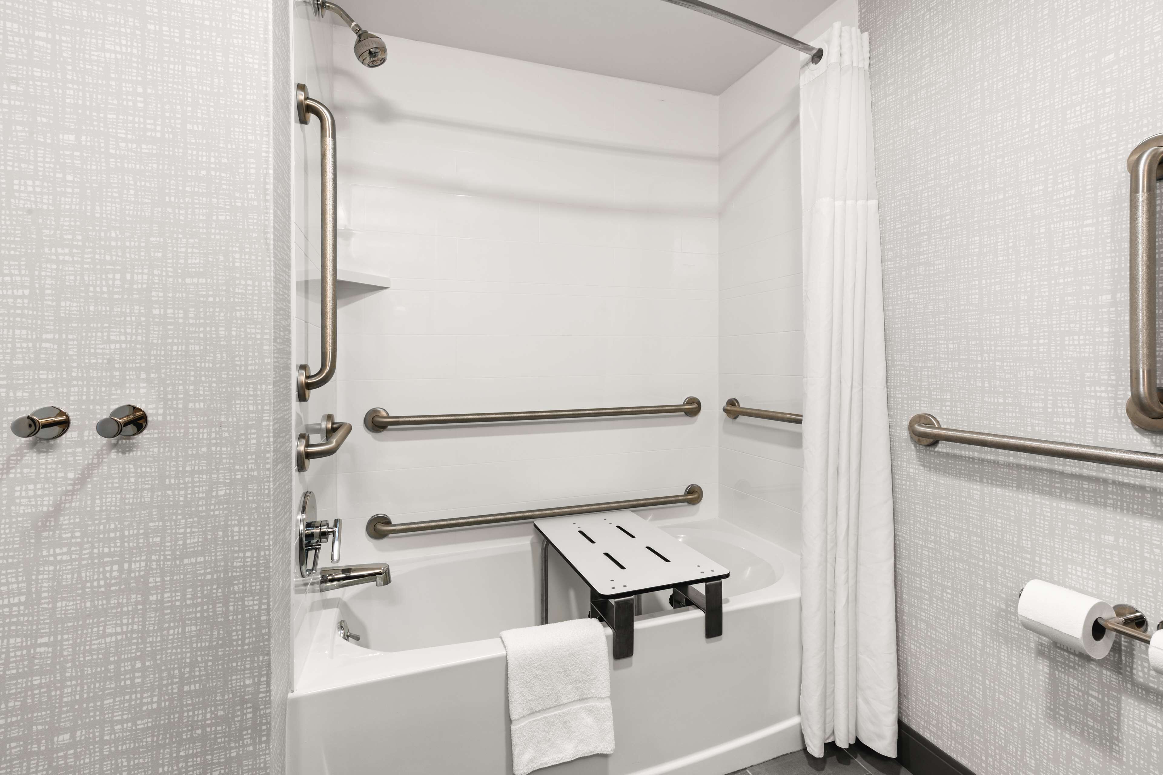 A modern bathroom with a bathtub, grab bars, a towel rack, and a toilet paper holder.