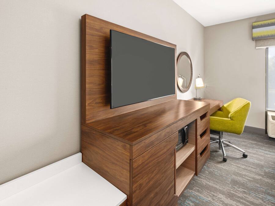 Ein modernes Hotelzimmer mit Schreibtisch aus Holz, einem Flachbildfernseher, einem gelben Sessel, einer Nachttischlampe und einem Fenster mit Blick.