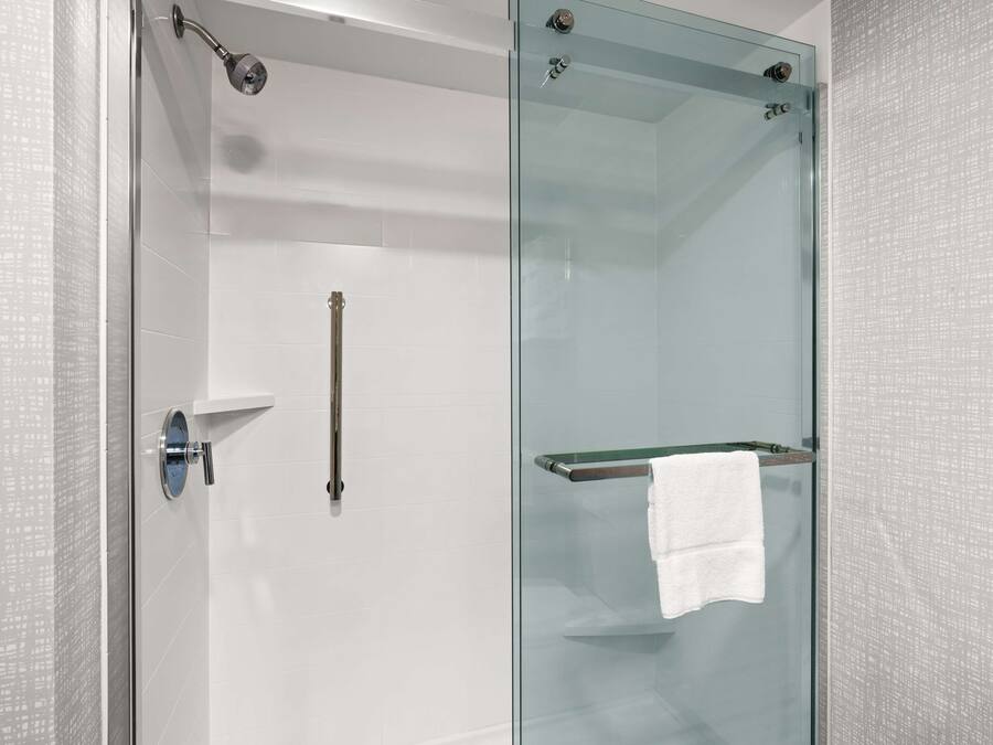 A modern bathroom with a glass shower enclosure, a white towel hanging on a rack, and a minimalist design.