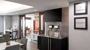 A modern hotel breakfast area with a counter, seating, and a TV screen.