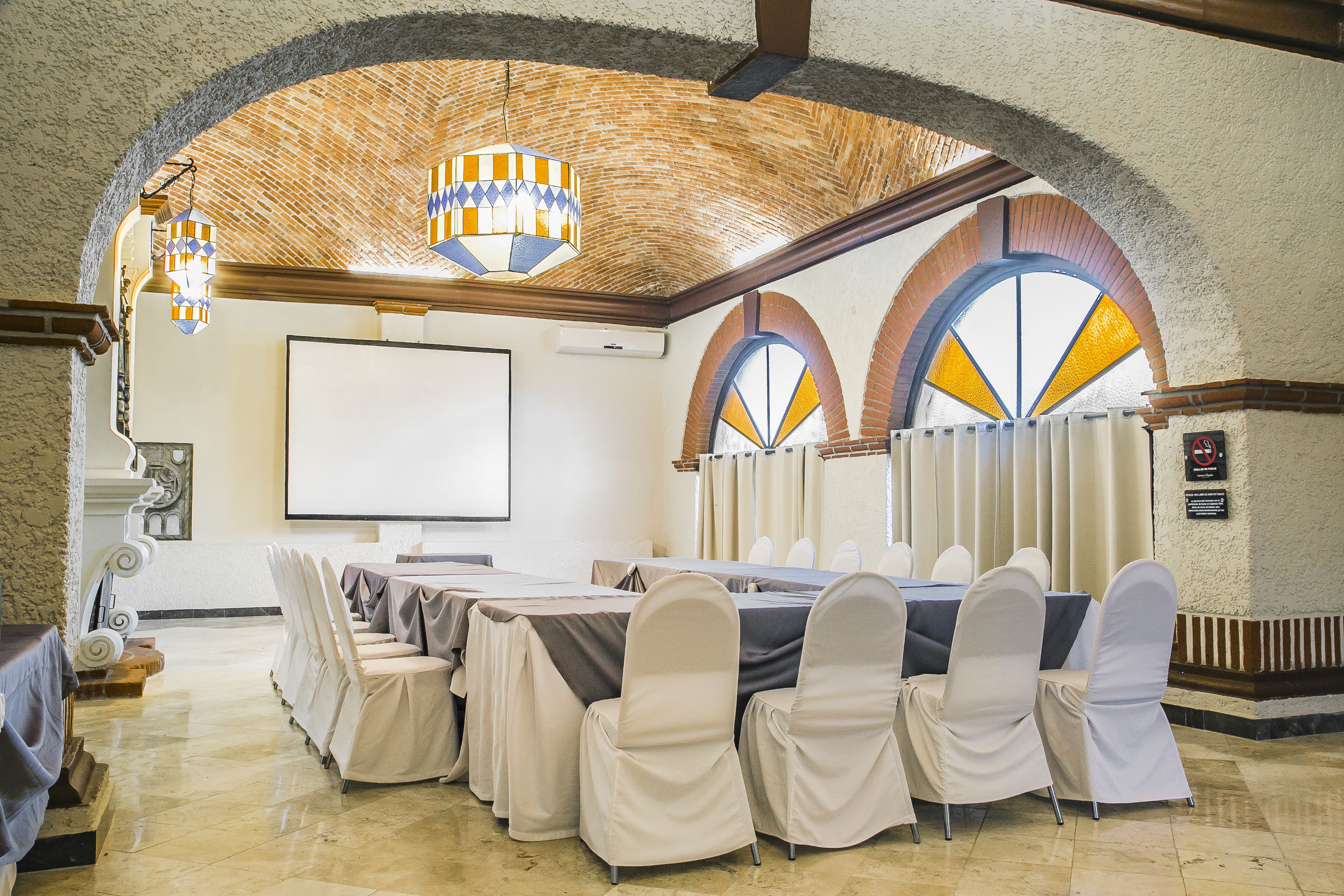 Un salón de conferencias con una larga mesa, sillas, una pantalla de proyector e iluminación decorativa.